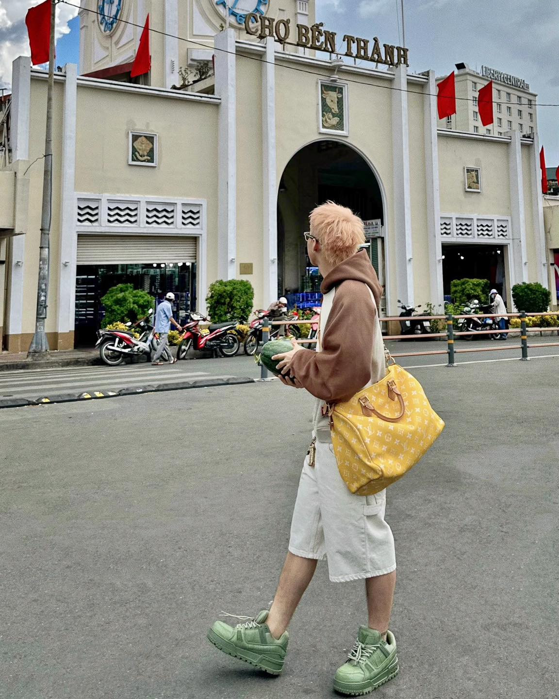 Anh kết hợp thêm túi Louis Vuitton màu vàng nổi bật và sneakers xanh cá tính, tạo nên tổng thể hài hòa nhưng vẫn rất bắt mắt.