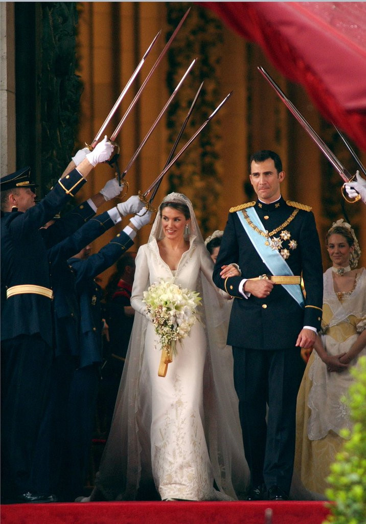 Hoàng hậu Letizia Ortiz trong lễ cưới với nhà vua Felipe VI của Tây Ban Nha và năm 2004. Váy cưới của bà được thiết kế bởi Manuel Pertegaz với kiểu dáng cổ lật tôn lên vẻ quyền lực và uy quyền của một bà hoàng.