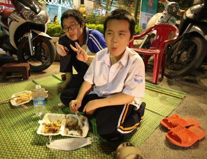 Một số học sinh được nghỉ học vào ngày mai (21/5) nên tự nguyện ra sân ngồi giữ chỗ. Các em được người nhà mang đồ ăn tiếp sức (Ảnh: Anh Thư)