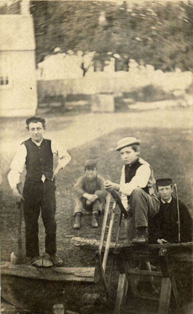 Một số người đàn ông dùng cưa và rìu để xẻ gỗ và bổ củi ở sân sau nhà.