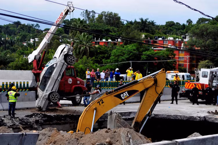Nhân viên cứu hộ sử dụng cần cẩu nhấc những chiếc xe lao vào hố trên đường cao tốc ở Cuernavaca, Mexico, ngày 12/7. Một người cha và con trai thiệt mạng khi hố này nuốt xe của họ vào sáng hôm đó. Hiện tượng "hố tử thần" xuất hiện ở bất cứ đâu và bất cứ khi nào. Thông thường, chúng phát triển một cách chậm rãi, nhưng cũng có khi bất ngờ cả hố lớn được hình thành. Ảnh: AP.