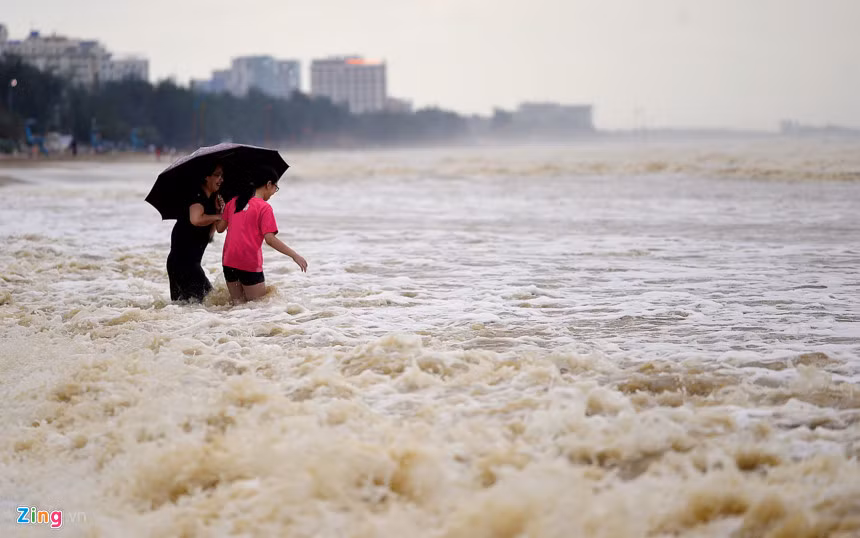 Khi nhiều người đã lên bờ, vẫn có một phụ nữ dắt theo bé gái tìm cách lội xuống biển trong mưa.