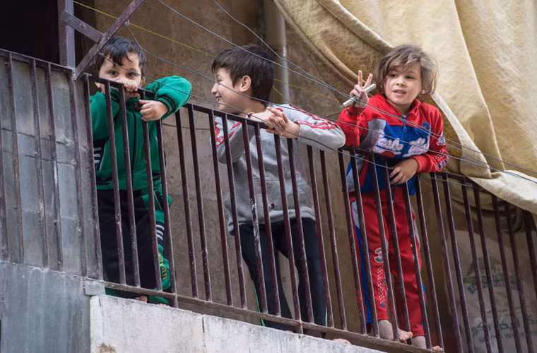 Những người lạ mới tới Aleppo đều trông thấy các ngôi nhà đổ nát, các con đường bị phong tỏa. Còn những trẻ em vui đùa gần đó.