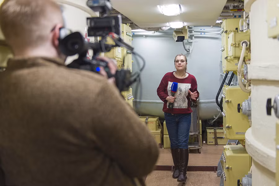 Nữ phóng viên Nga đang đi trong tàu ngầm, có thể là gần khu vực đặt ống phóng thẳng đứng tên lửa đạn đạo.