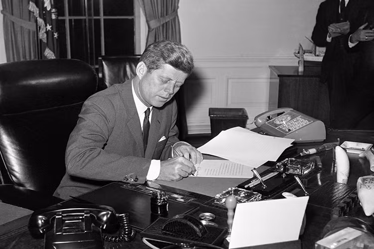 Không gian bàn làm việc của cựu Tổng thống John F. Kennedy vào năm 1962 có vẻ khá chật chội với vô số các vật dụng và có tới hai chiếc điện thoại được đặt trên Chiếc bàn Kiên Định. Ảnh: Business Insider.