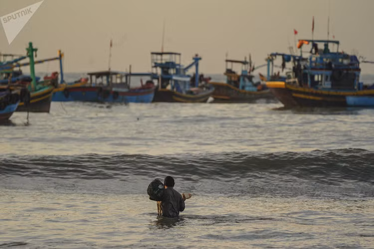Một ngư dân Bình Thuận lội sóng để ra con tàu của mình. Ảnh: Sputnik.