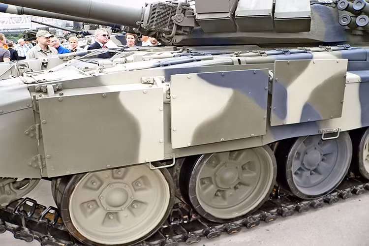 Có thể dễ dàng nhận thấy phiên bản T-90A mà chính Quân đội Nga đang sử dụng không hề có giáp phản ứng nổ bao bọc bên hông, thậm chí còn chẳng được tăng cường tấm chắn xích với nhiều tấm thép composite như những chiếc chiến xa khác mà chỉ có vỏn vẹn 3 miếng thép mỏng gắn khá tạm bợ vào phía trước. Nguồn ảnh: Thai Military.