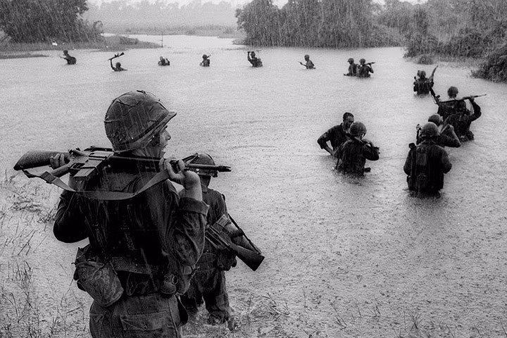 Yếu tố thời tiết và địa hình là trở ngại lớn đối với lính Mỹ. Trong ảnh, lính dù Mỹ vác súng lội sông trong lúc trời mưa tầm tã để tìm diệt các vị trí của quân cách mạng, vào năm 1965. Ảnh: AP.