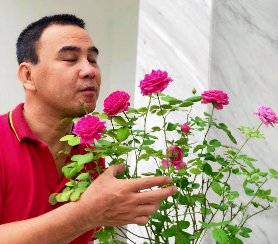 Quyền Linh vui vẻ tạo dáng bên khóm hoa hồng.