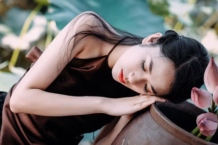 Hình ảnh thí sinh Hoa hậu Việt Nam 2018 mặc áo yếm tạo dáng bên hoa sen trong một bộ ảnh.