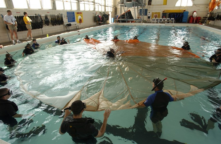 Bài tập giải cứu nạn nhân bị mắc kẹt trong dù ở dưới nước của các nhân viện cứu hộ không quân hải quân. Dù chính là kẻ thù số một của các phi công khi họ nhảy dù xuống biển, dù có thể quấn quanh người phi công khiến anh ta chết đuối nếu không giữa được bình tĩnh để thoát khỏi "mớ bòng bòng" này. Nguồn ảnh: Wiki.