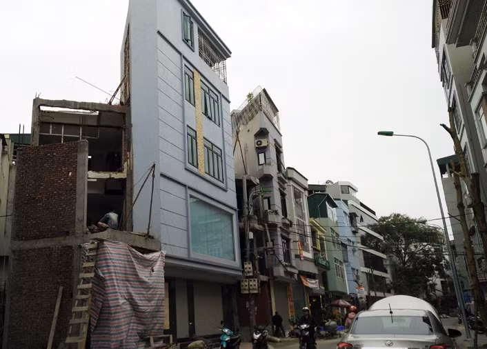 Hai ngôi nhà siêu mỏng, siêu méo với cạnh hình tam giác đã hoàn thiện và ngay gần đó là một nhà khác đang trong quá trình xây dựng.