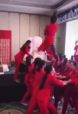 Theo đó, người đứng ở phía trên bục khá cao, những người ở dưới đan tay đỡ đều là phụ nữ nên sức đỡ không quá lớn. Do lực thả rơi quá mạnh và nhanh nên gần như không thể đỡ được, người phụ nữ rơi thẳng xuống đất ôm đầu đau đớn.