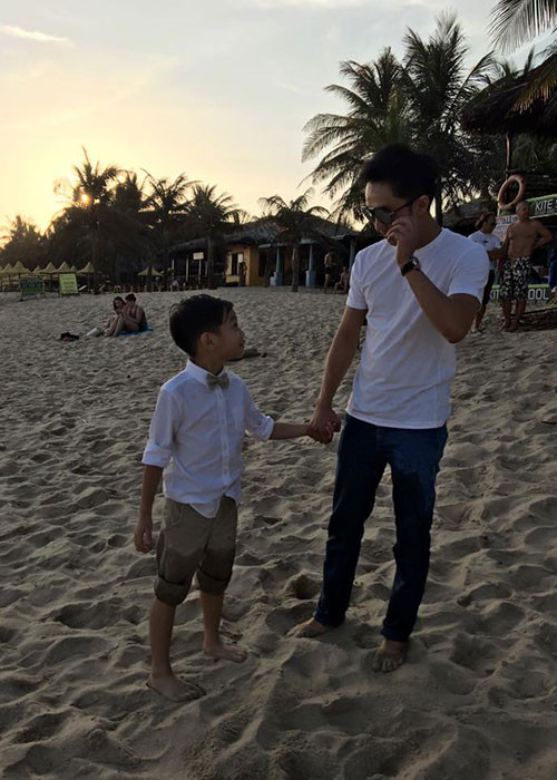 Cường Đô-la và con trai đều diện áo trắng và nắm tay nhau vô cùng tình cảm khi dạo chơi trên bờ biển.