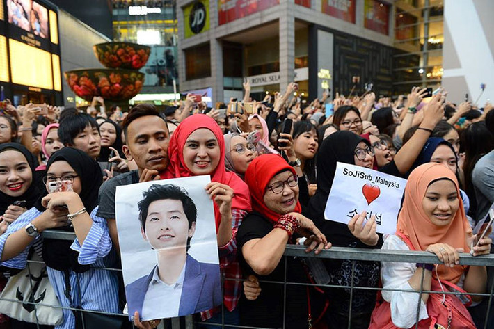 Người hâm mộ Malaysia giơ hình ảnh thần tượng. Dễ dàng nhận ra có rất nhiều người hâm mộ lớn tuổi xếp hàng chờ đón.