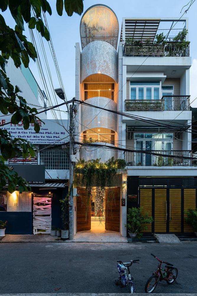 Có mặt tiền chỉ bằng 1/2 những ngôi nhà bên cạnh, gia chủ của ngôi nhà trong hình cho lùi các khối chức năng về phía sau một chút rồi ở mỗi tầng bố trí một mái vòm hình nan sắt có lỗ, tạo ra sự khác biệt cho ngôi nhà. Ở tầng 2 còn trồng thêm nhiều cây cảnh và dây leo để tạo điểm nhấn và giúp không khí trong nhà mát mẻ và trong lành hơn.
