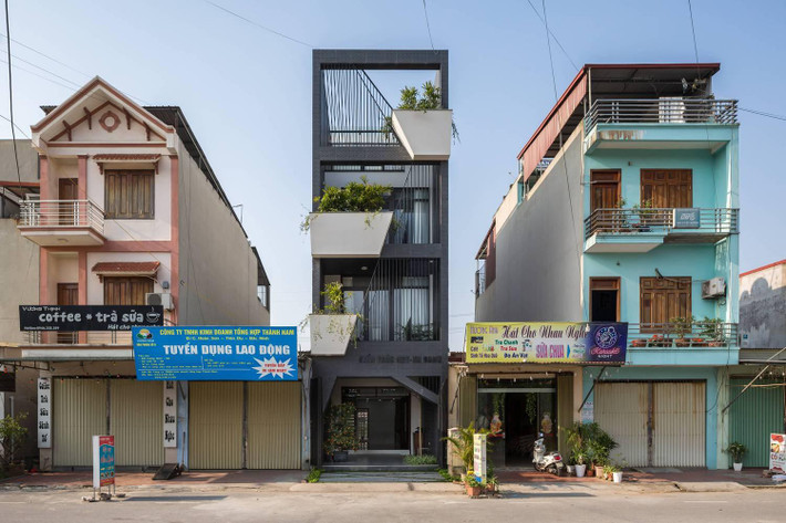 Sử dụng màu sơn ngoại thất màu đen khói và các nan sắt cùng màu làm mặt tiền cho căn nhà ống bị kẹp giữa nhiều ngôi nhà khác là một thiết kế được khá nhiều người ưa chuộng trong năm 2021. Điểm nhấn của thiết kế này là tạo ra các khối bê tông có hình chậu cây với kích thước và vị trí khác nhau ở mỗi tầng, sơn nó màu trắng rồi trồng cây xanh ở mặt tiền ngôi nhà, tạo ra điểm nhấn giữa một tổng thể màu đen.