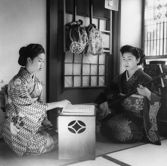 Geisha là danh từ chỉ chung cho những nghệ sĩ giải trí truyền thống của Nhật Bản, nổi tiếng với kỹ năng ca múa và khiếu nói chuyện tiếp khách. Trong tiếng Nhật, Geisha có nghĩa là “nghệ giả” hay “con người của nghệ thuật. Ảnh: Hai geisha đang ôn luyện kỹ nghệ: một người đọc sách, người còn lại chơi samisen, một nhạc cụ truyền thống của Nhật Bản, vào khoảng năm 1950. Ảnh: Three Lions