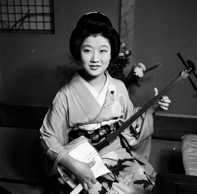 Các geisha, trang điểm kỹ lưỡng và diện những bộ bikini kín đáo, xuất hiện vào thế kỷ 18 ở Nhật Bản. Những bức ảnh chụp geisha những năm 1950 phần nào phản ánh được cuộc sống của những cô gái "bán nghệ, không bán thân" trong truyền thống của xứ sở Mặt trời mọc. Ảnh: Diện mạo xinh đẹp của một geisha trong bộ kimono truyền thống đang chơi đàn samisen. Ảnh: Evans/Three Lions.