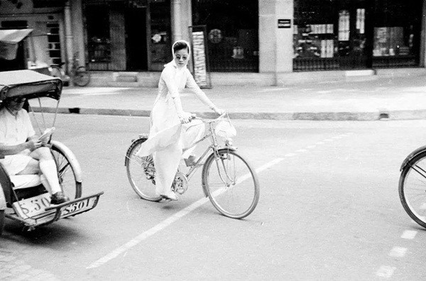 Một cô gái mặc áo dài trắng, đeo khăn trắng và tạo điểm nhấn bởi cặp kính đen, trông không khác nào một bức ảnh bìa của tạp chí Vogue Pháp. Cách kết hợp đồ đầy thanh lịch khiến người phụ nữ trở nên quý phái dù đang đạp xe đạp.