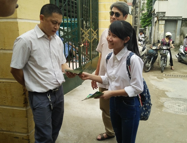 Cô gái phát tờ rơi cười nói vui vẻ chào mời người nhận, phụ huynh thì nhăn mặt, khó chịu vì phải cầm quá nhiều.