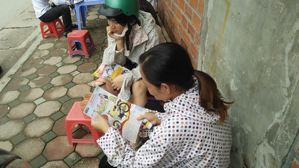 Một số phụ huynh đọc tờ rơi "giết" thời gian trong lúc chờ con.