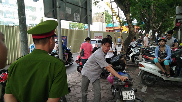 Một chiến sĩ cảnh sát nhắc nhở phụ huynh đưa con đi thi xếp xe gọn gàng để không gây cản trở giao thông. Ảnh chụp tại điểm thi Đại học Sư phạm Hà Nội.