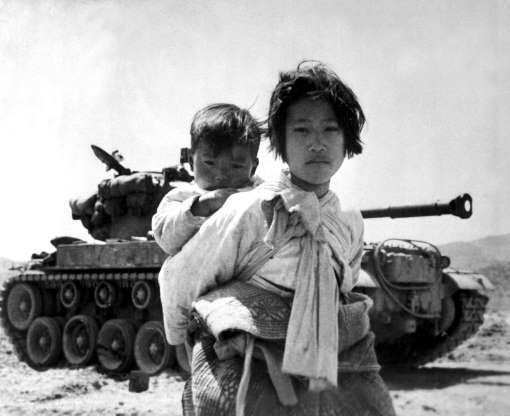 Một bé gái cõng em đi qua chiếc xe tăng M-26 bị chết máy, tháng 6/1951.