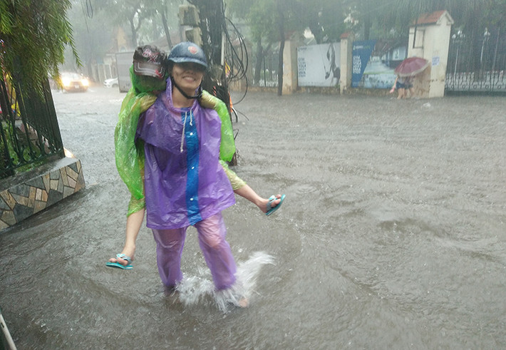 Nước ngập sâu làm em nhỏ không thể đi bộ qua được, và phải nhờ phụ huynh cõng.
