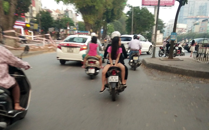 Một bé gái khoảng 6 tuổi, ngồi ngược vắt vẻo sau xe máy của mẹ trên đường Láng (Đống Đa, Hà Nội). Trong khi đó, mật độ phương tiện tham gia giao thông vào thời điểm này rất đông, tiềm ẩn tai nạn đe dọa bé gái.