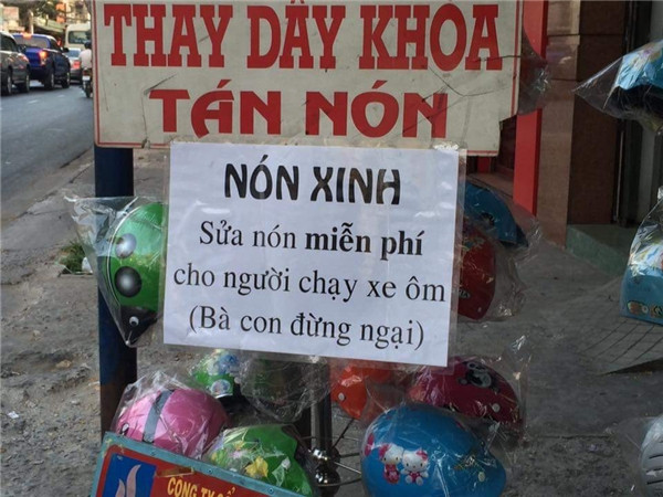 Cửa hàng mũ bảo hiểm kèm "dịch vụ" sửa mũ bảo hiểm miễn phí cho người chạy xe ôm. Người chủ tiệm còn khéo léo nhắc nhở "Bà con đừng ngại" để việc làm của mình tăng thêm phần ý nghĩa.