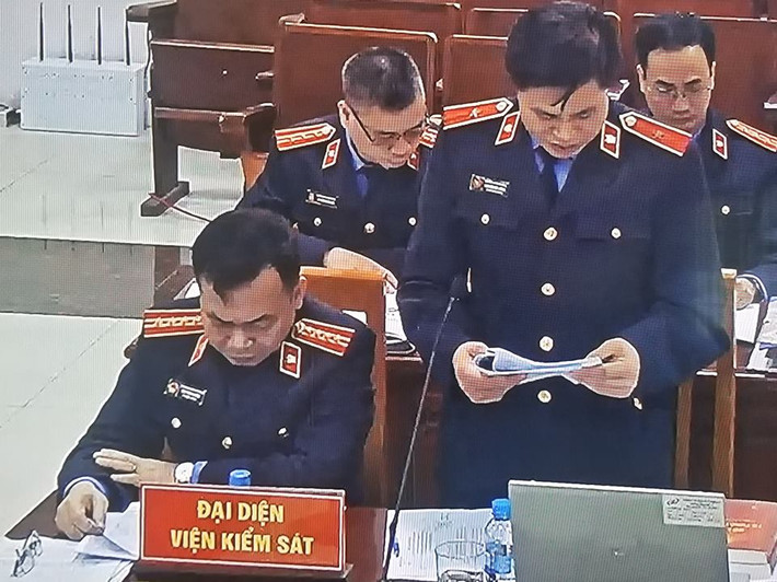 Sau khi kết thúc phần xét hỏi căn cước, đại diện VKSND TP Hà Nội đứng dậy công bố bản cáo trạng dài 25 trang truy tố cựu hai Thứ trưởng Bộ Công an Bùi Văn Thành và Trần Việt Tân. (Ảnh chụp qua màn hình).