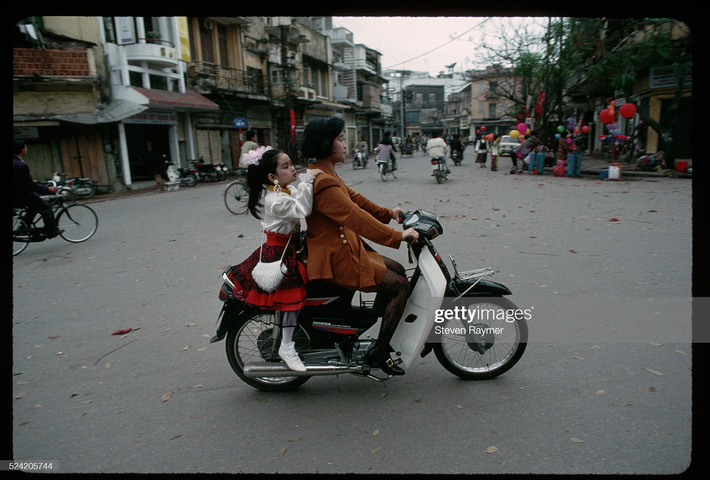 Trên một con phố ở Hà Nội, bà mẹ đèo cô con gái xúng xính trong bộ váy áo mới ngày Tết, đường sá thưa thớt người và những căn nhà mang một màu cổ kính. Ảnh: Steven Raymer.