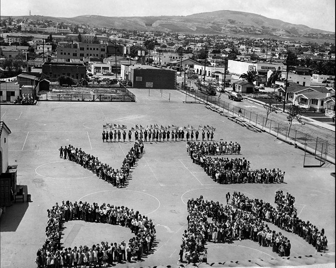 Học sinh trường Fifteenth Street ở San Pedro, bang California, Mỹ xếp hình chữ VE DAY (Ngày Chiến thắng) trên sân trường vào ngày 7/5. Các giáo viên cầm cờ và đứng phía sau. Ảnh: Los Angeles Times.