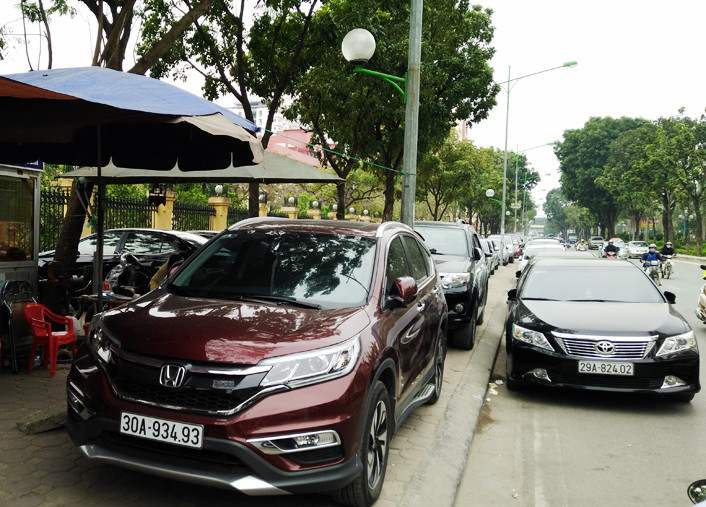 Các xe ô tô xếp hàng dài trên vỉa hè và dưới lòng đường tại điểm trông giữ xe cổng Học viện Chính trị Quốc gia Hồ Chí Minh.