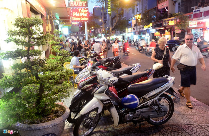 Tối 22/2, thời điểm thành phố vừa lên đèn, các cơ sở kinh doanh khách sạn, ăn uống, hàng quán... ở nhiều tuyến đường thuộc quận 1 vẫn lấn chiếm nhiều đoạn vỉa hè bằng cách dựng xe máy, bày đồ ăn. Trong ảnh, một khách sạn trên đường Lê Thánh Tôn ngoài việc bày hai chậu cây cảnh còn cho khách để xe máy chiếm gần hết vỉa hè.