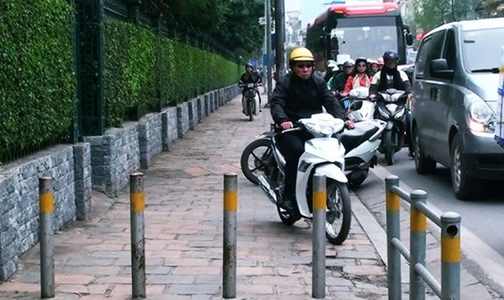 Một số xe máy định leo lên vỉa hè nhưng bị hàng rào barie ngăn lại.