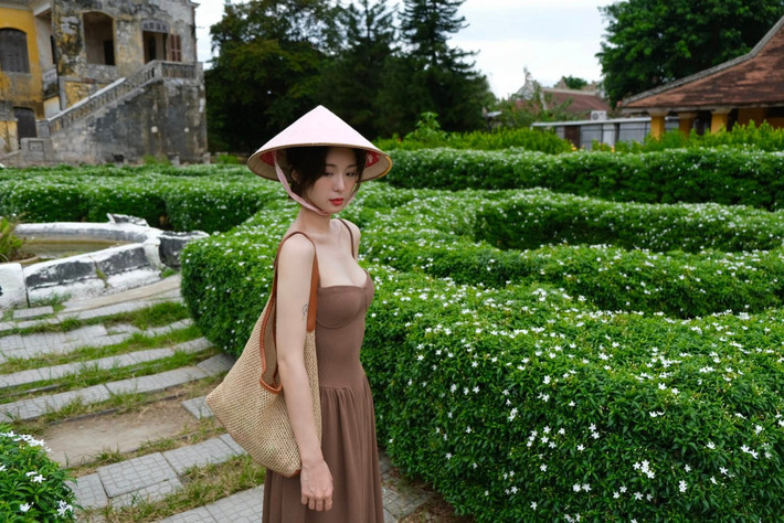 Điểm nhấn không thể thiếu là chiếc nón lá truyền thống, che hờ gương mặt thanh tú, tạo nên vẻ đẹp bí ẩn và đầy chất thơ.