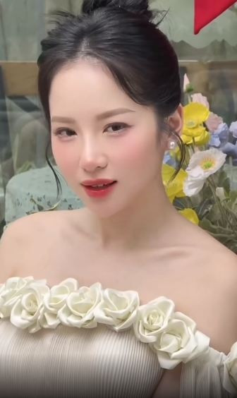 Vẻ đẹp ngọt ngào của Loan Barbie càng được tôn lên nhờ lối trang điểm nhẹ nhàng với má hồng, môi đỏ cam và kiểu tóc búi cao gọn gàng.