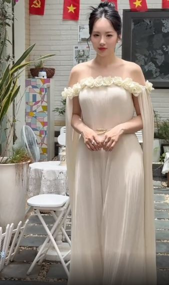 Trong đoạn video, Loan Barbie diện chiếc đầm trễ vai màu kem nhã nhặn, được điểm xuyết bằng dải hoa hồng nổi tinh tế dọc phần ngực và vai.