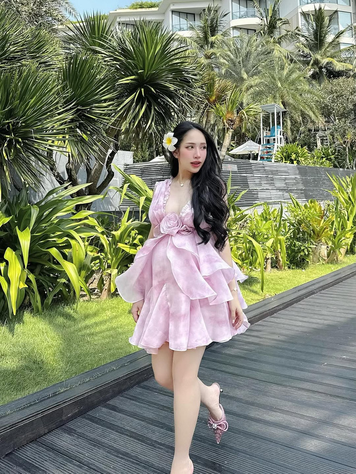 Dù bụng bầu vượt mặt nhưng Joyce Phạm vẫn tự tin mang giày cao gót để thấp với màu hồng cùng tone với váy. Cô cũng khéo léo kết hợp phụ kiện đậm tính nhiệt đới như bông hoa sứ cài tóc.