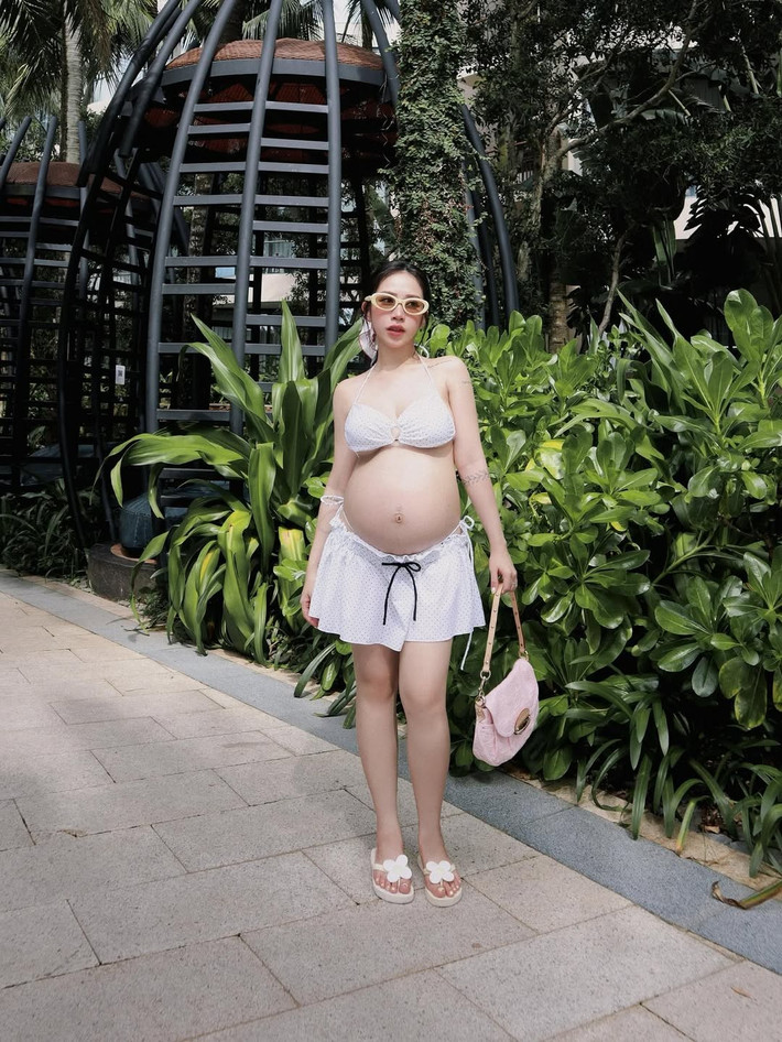 Trong loạt ảnh được chia sẻ, Joyce Phạm đã chứng minh rằng mẹ bầu vẫn có thể vô cùng quyến rũ và thời thượng. Cô nàng tự tin diện những bộ bikini đa dạng, trong bộ ảnh mới nhất, con gái Minh Nhựa diện set bikini chấm bi trắng tinh khôi đi kèm chân váy ngắn cùng tông.