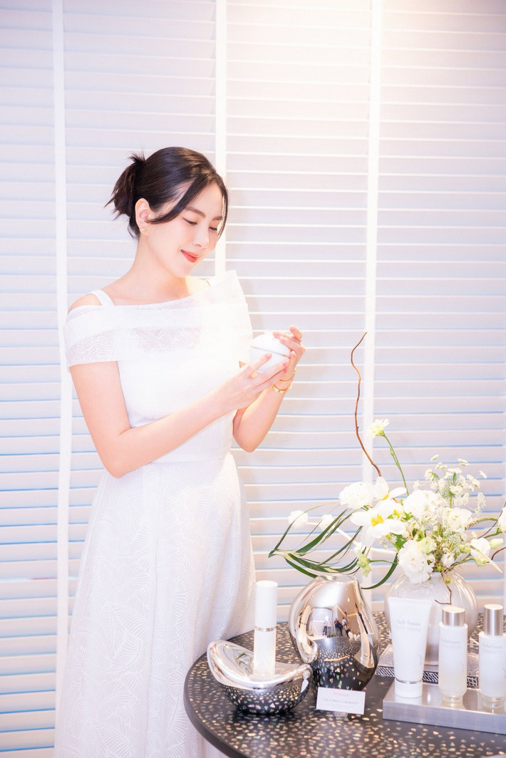Nữ MC lựa chọn một chiếc đầm trắng dáng dài, thiết kế trễ vai nhẹ nhàng, tôn lên bờ vai thanh thoát và vòng eo thon gọn. Bộ trang phục cùng lối trang điểm tự nhiên, mái tóc búi cao đơn giản nhưng vẫn toát lên vẻ đẹp thanh lịch, sang trọng và đầy cuốn hút.