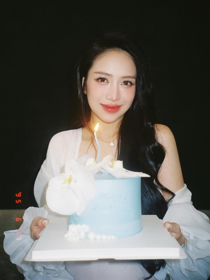 Đặc biệt, chiếc bụng bầu "vượt mặt" của cô là tâm điểm, thể hiện niềm hạnh phúc và sự mong chờ chào đón thành viên mới của gia đình. Hình ảnh Joyce Phạm ngồi bên chiếc bánh sinh nhật màu xanh nhạt, trên đó có trang trí những bông hoa lan trắng tinh tế, càng làm tăng thêm chất điện ảnh.