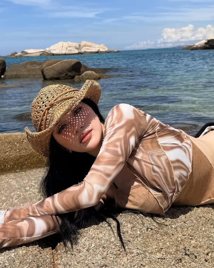Trong loạt ảnh mới, Sĩ Thanh diện bộ trang phục phối tinh tế giữa phong cách gợi cảm và phóng khoáng. Phần áo dài tay ôm sát cơ thể, kết hợp cùng váy lụa trắng suông nhẹ và chiếc nón cói bản to mang đậm hơi thở biển cả, vừa tạo cảm giác mềm mại, bay bổng, vừa tôn lên từng đường cong quyến rũ.
