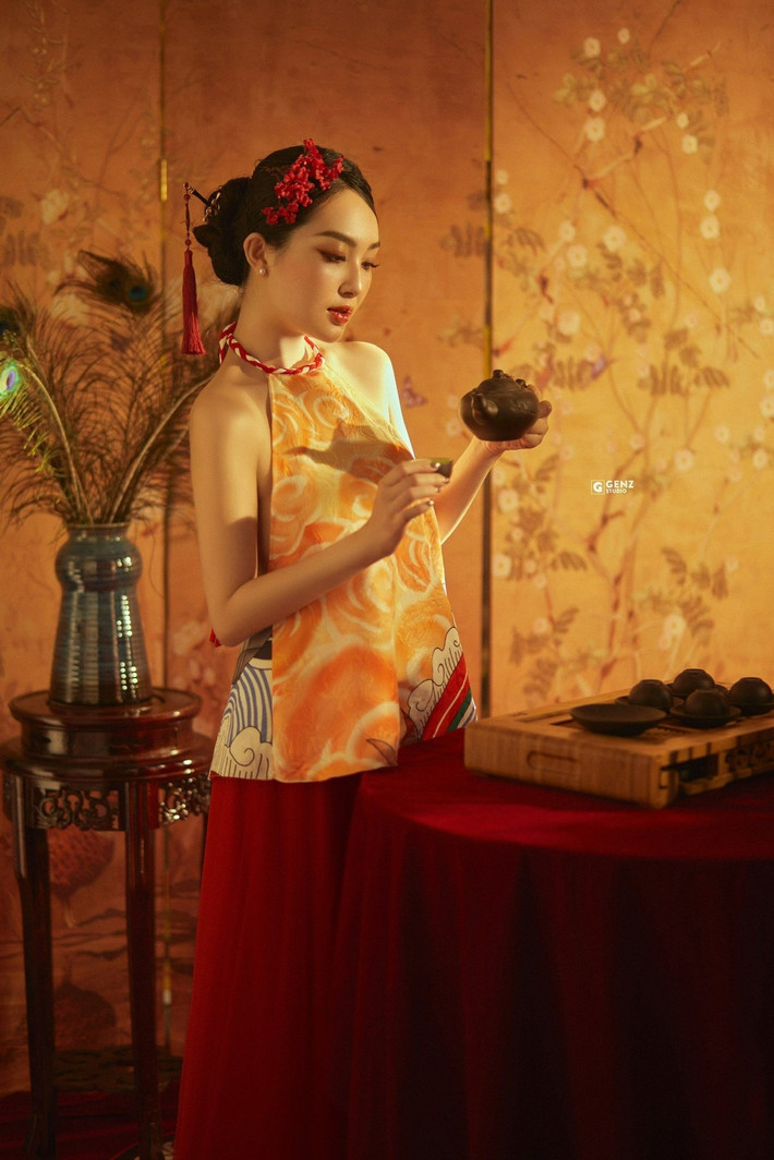 Bối cảnh chụp với ánh sáng vàng ấm áp, tấm bình phong họa tiết hoa đào, cùng bình hoa cắm lông công và bộ trà cụ, tất cả đã tái hiện thành công một không gian Tết Đoàn Viên đầm ấm, lãng mạn và đầy hoài niệm. (Ảnh: FBNV)