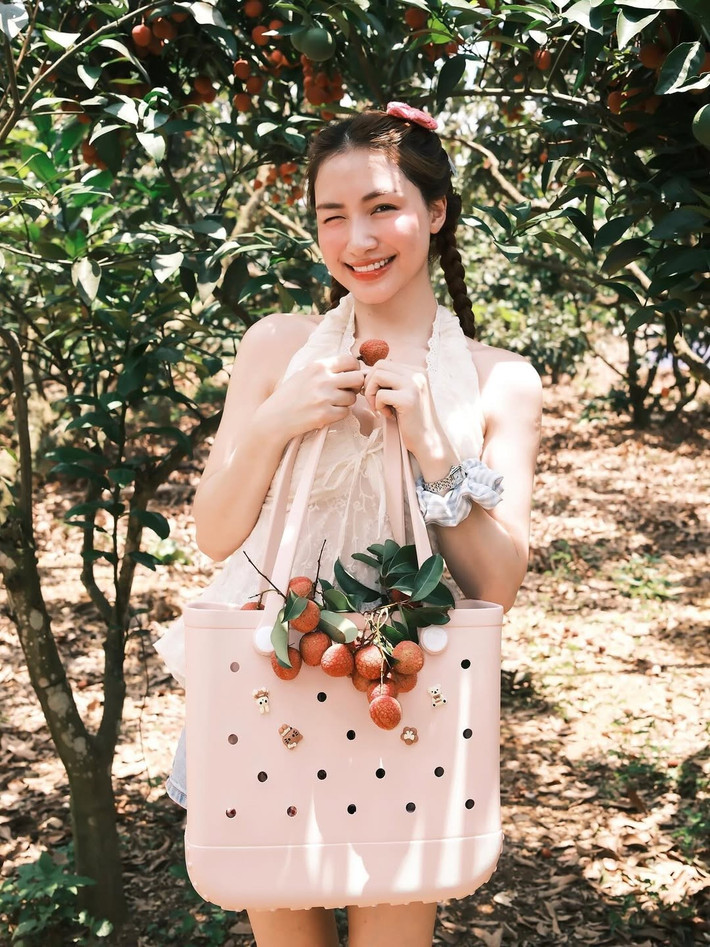 Trong một bức ảnh, Hòa Minzy cười tươi rạng rỡ, nháy mắt tinh nghịch khi cầm trên tay chùm vải chín mọng, như đang mời gọi người xem cùng thưởng thức. Nụ cười "thương hiệu" của cô nàng với đôi mắt híp lại và khóe miệng duyên dáng luôn là điểm sáng, mang đến năng lượng tích cực cho người đối diện.