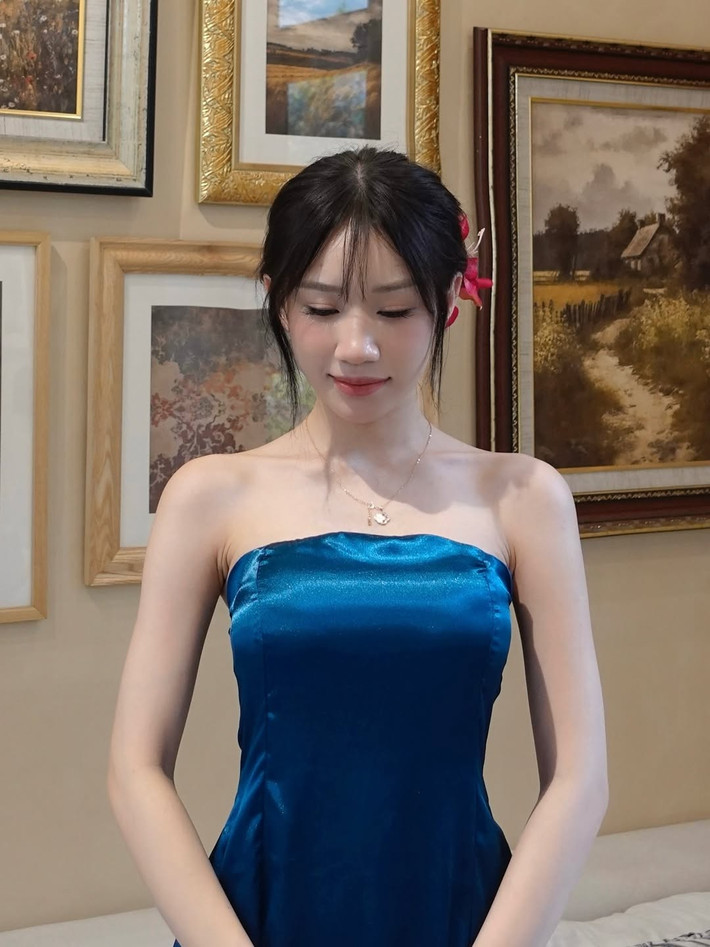 Mái tóc búi cao gọn gàng, cài hoa lớn màu hồng rực tạo cảm giác nữ tính và tinh tế, như một nhân vật bước ra từ tranh vẽ.