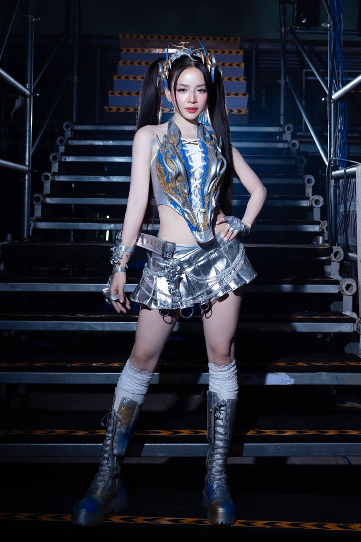 Phần thân trên là một chiếc corset ôm sát, được trang trí bằng các họa tiết cầu kỳ, kết hợp cùng chân váy mini xếp ly ánh bạc, tạo nên vẻ ngoài vừa quyến rũ vừa đầy mạnh mẽ.