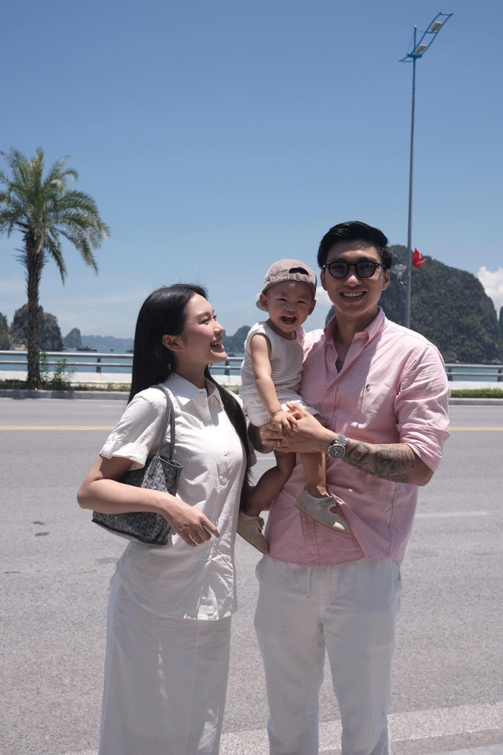 Cả hai đều chọn trang phục đơn giản, thoải mái. Cậu con trai nhỏ cũng diện trang phục tone trắng, được Đoàn Văn Hậu bế trên tay, cười tươi vui vẻ.